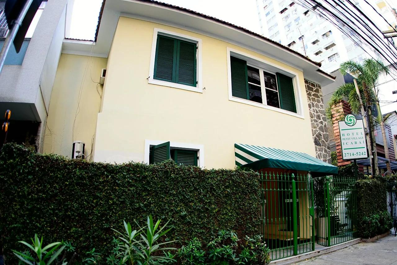 Fachada do Hotel Petit Village Icaraí: casarão amarelo com janelas verdes, toldo listrado e jardim na frente